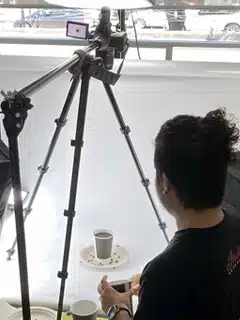 Una persona de una agencia de marketing en CDMX está colocando una cámara en un trípode para fotografiar una taza colocada sobre un fondo blanco.