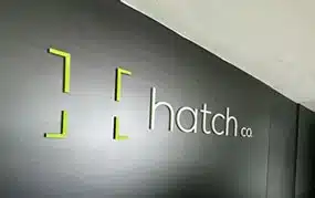 Una pared que muestra el logotipo "Hatch Co." con un diseño de dos corchetes verdes sobre fondo negro, mostrando su experiencia en servicios de marketing.