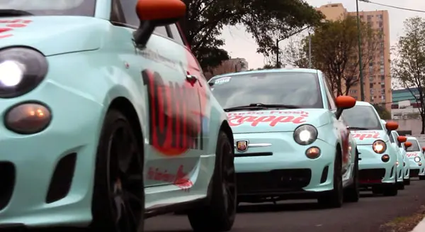 Una fila de automóviles Fiat 500 de color azul claro con espejos laterales de color naranja, marcados con "Guappi", se alineaban en las calles de una zona urbana, parte de una vibrante activación de marca en CDMX.