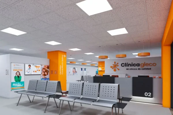 Una moderna sala de espera clínica con decoración naranja y gris, con filas de sillas grises y carteles informativos alineados estratégicamente en las paredes, encarna la estrategia de comunicación de Glecolab, con un elegante mostrador de recepción al fondo.